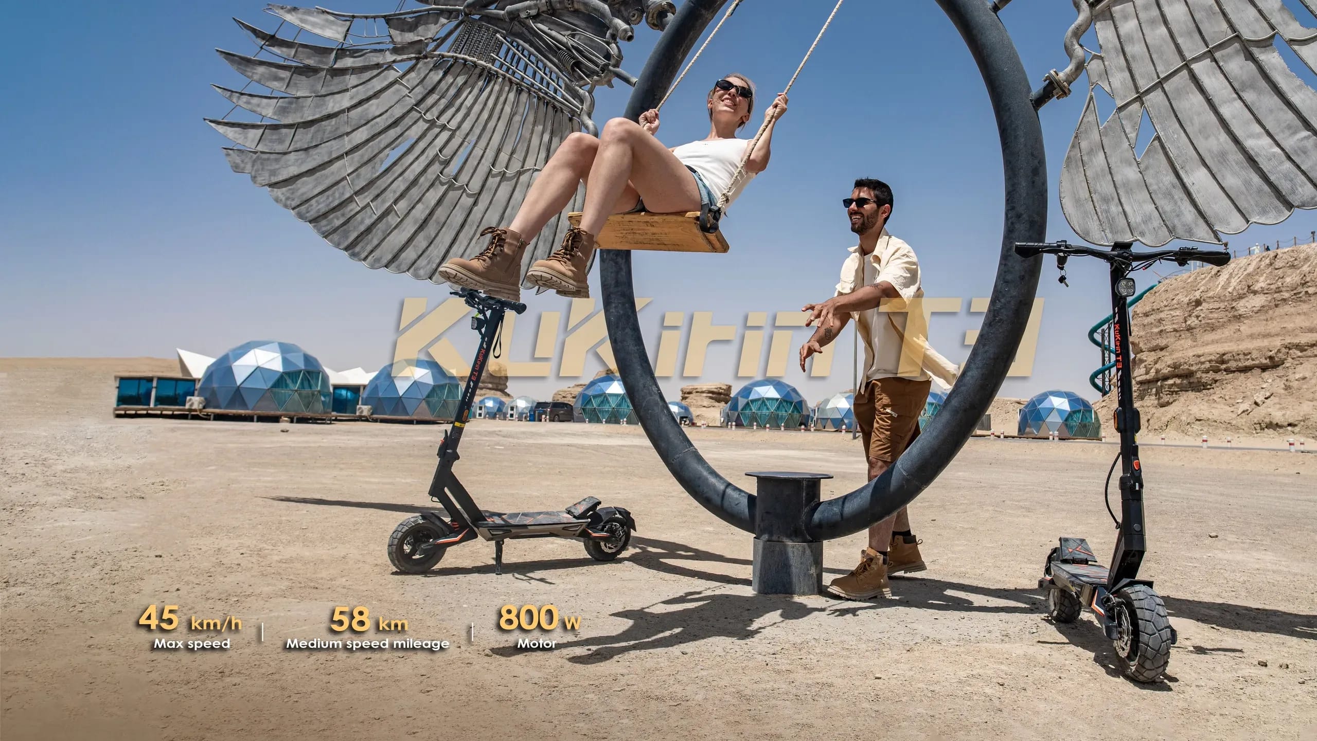 Two people enjoy a swing ride and electric scooters at a futuristic desert retreat.